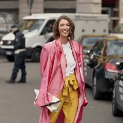 Mujer sonriente con abrigo rosa y pantalones amarillos, demostrando los **colores que combinan con amarillo** en un día urbano.