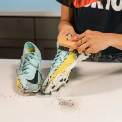 Manos cepillando unas botas de fútbol sucias para aprender como lavar las botas de futbol.