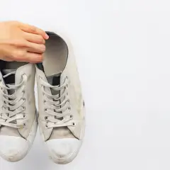 Mano sosteniendo un par de zapatillas blancas de tela sucias, listas para limpiar.