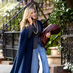 Estilo chic en la ciudad: una mujer con un abrigo azul marino y falda vaquera, combinando granate y verde con su bolso y el follaje.