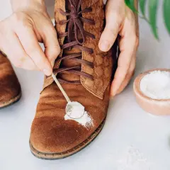 Manos aplicando polvo blanco con una cuchara sobre un zapato de gamuza marrón.