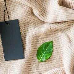 Etiqueta negra sobre tejido beige, con una hoja verde al lado. Símbolo de una marca sostenible.