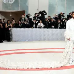 Bad Bunny deslumbra en la Met Gala con un traje blanco adornado con flores, rodeado de fotógrafos.