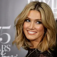 Mujer sonriendo con pelo rubio ondulado a la altura de los hombros y maquillaje.