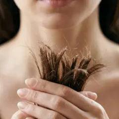 Mano sosteniendo mechón de pelo seco y rebelde. Descubre cómo quitar el frizz del pelo para un acabado suave y sedoso.