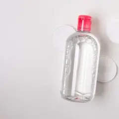 Botella de agua micelar con tapa rosa y discos de algodón. Ideal para limpiar ante y rostro.