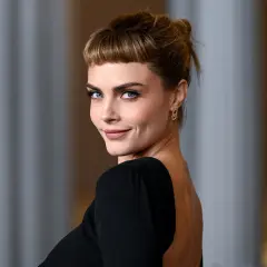 Cara Delevingne, con su mirada penetrante y un peinado recogido con flequillo, luce un elegante vestido negro de espalda descubierta.