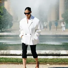Mujer con un elegante outfit con leggins negro y blazer blanco, paseando cerca de una fuente.