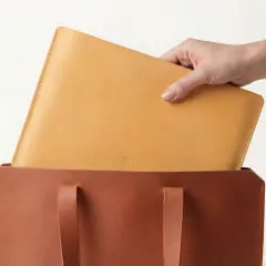 Mano colocando un portátil de piel vegetal en un bolso de cuero.