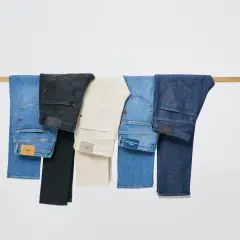 Cinco tipos de pantalones, incluyendo vaqueros azules, negros y beige, colgados en una barra de madera.