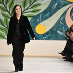Maria Grazia Chiuri camina en la pasarela con un traje negro, sonriendo ante el público aplaudiendo.
