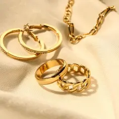 Anillos y cadena dorados sobre tela. Los aros tienen pequeñas piedras preciosas incrustadas, como si fueran diamantes.