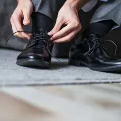 Man se ata los cordones de sus zapatos de piel negros, preparándose para evitar rozaduras.
