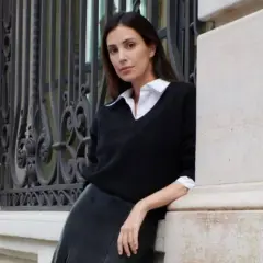 Sassa de Osma, elegante con jersey negro y falda de cuero, apoyada en una columna de piedra junto a una reja ornamental.