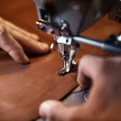 Manos cosiendo con precisión una pieza de cuero vegetal en una máquina de coser industrial.