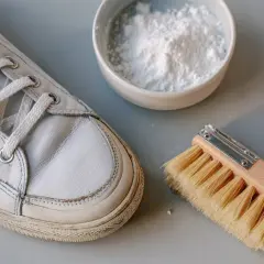 Herramientas para limpiar botines blancos: un zapato, un cepillo y un cuenco con polvo blanco.