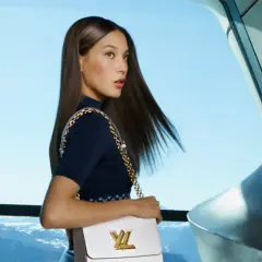 Eileen Gu, con su bolso Louis Vuitton, posa con elegancia frente a un paisaje montañoso y un cielo azul.