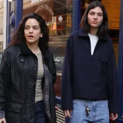 Dos jóvenes pasean por una calle, uno con chaqueta negra y el otro con jersey azul marino. Quizás buscando la loli bahía.