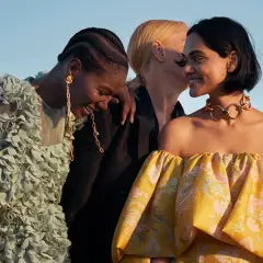 Tres mujeres ríen, una con un vestido verde con flores, otra con un collar dorado y un vestido amarillo estampado. Moda ecofriendly que es.