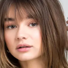 Chica con flequillo desfilado y cabello castaño, ideal para cortes de pelo para cara redonda.