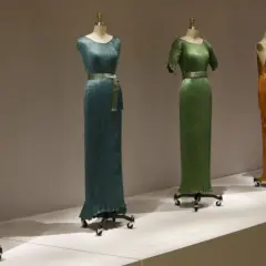Cinco vestidos Delphos en tonos vibrantes: naranja, azul, verde, amarillo y rojo, exhibidos en maniquíes.