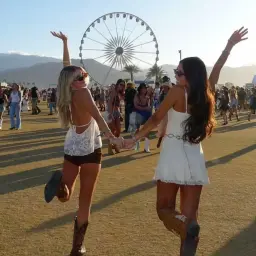 Dos amigas celebran la música y la moda en Coachella, con la noria de fondo y un ambiente festivo.