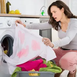 Mujer sorprendida al ver su ropa blanca manchada de rosa tras la lavadora. ¡Un desastre para quitar desteñidos en ropa de color!