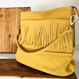 Bolso amarillo de ante con flecos, apoyado sobre una caja de madera. Un diseño bohemio que evoca el estilo del ante.