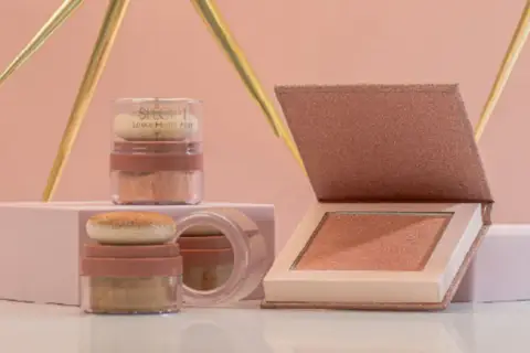 Dos envases de iluminador sueltos y un iluminador en polvo compacto, todos con tonos dorados y rosados, listos para dar luz a tu rostro.
