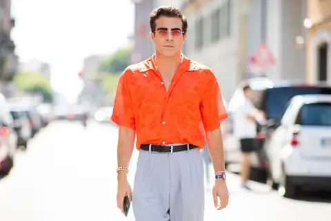 Hombre con camisa naranja estampada y pantalones grises, luciendo un elegante french tuck.