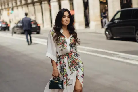 Mujer con vestido estampado floral, estilo manga francesa, pasea por París con un bolso verde.
