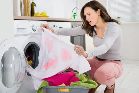 Mujer sorprendida al ver su ropa blanca manchada de rosa tras la lavadora. ¡Un desastre para quitar desteñidos en ropa de color!