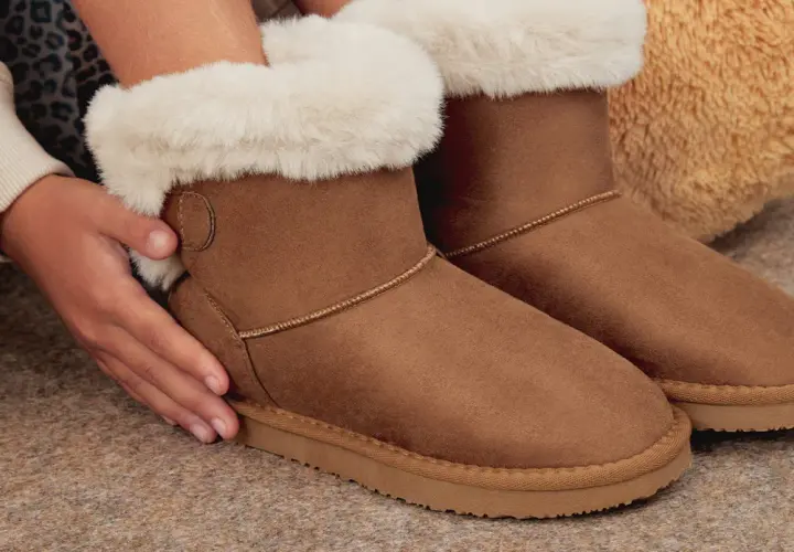 Manos cuidando unas botas de pelo marrones, perfectas para aprender como limpiar botas de pelo y mantenerlas como nuevas.