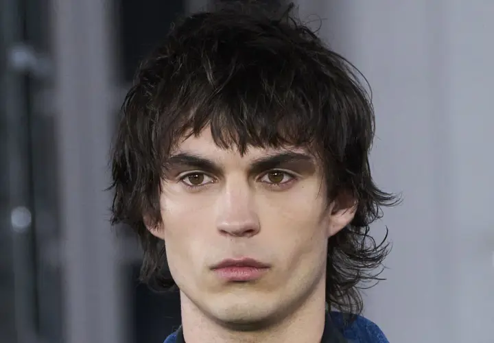 Joven con un moderno corte mullet, cabello oscuro y despeinado, mirada intensa y cejas marcadas.