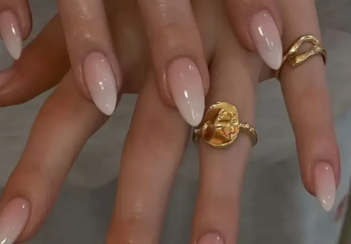 Manos con uñas baby boomer natural, un degradado suave de rosa a blanco. Dos anillos dorados adornan los dedos.