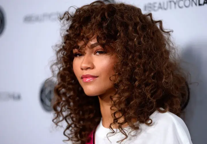 Mujer con cabello castaño rizado y flequillo, un ejemplo de cortes de pelo rizado que realzan su belleza natural.