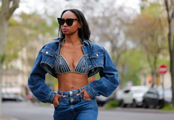Mujer con gafas de sol luce un conjunto de **denim on denim**: chaqueta corta y sujetador de pedrería, combinados con jeans.