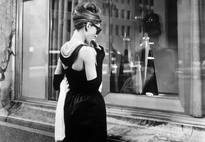 Audrey Hepburn, icónica en su vestido negro y perlas, disfruta de un pastel frente a Tiffany's.