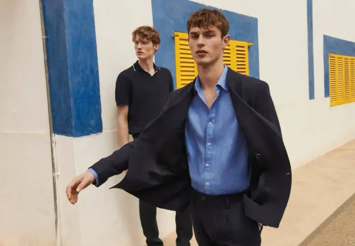Dos hombres modelan un outfit oficina verano hombre: uno con chaqueta azul marino y camisa de lino, otro con polo oscuro.