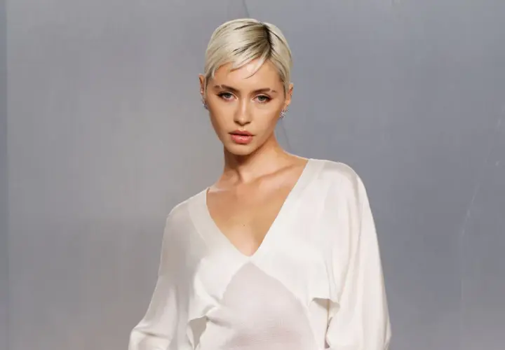 Iris Law, con su corte de pelo rubio platino y un top blanco de seda, posa con una mirada intensa.