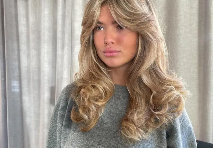 Mujer con cabello rubio y ondas voluminosas, un corte **hush cut** que enmarca su rostro.