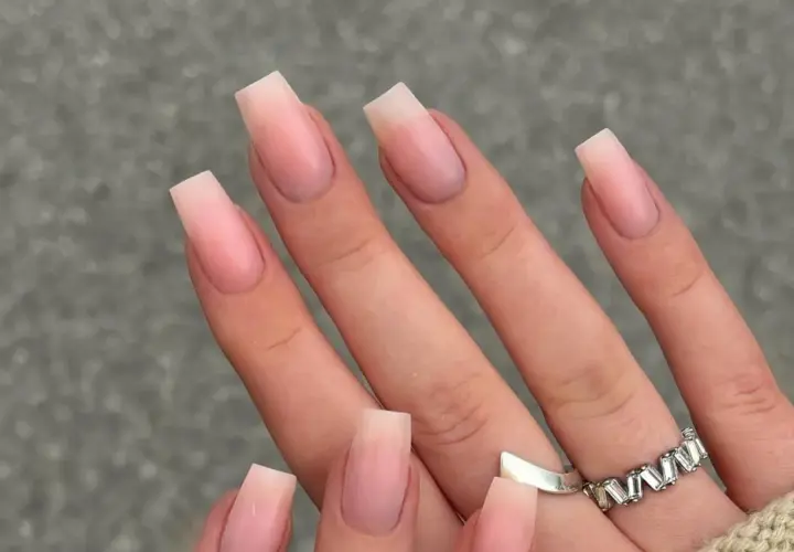 Manos con uñas naturales bonitas en forma cuadrada, con un degradado sutil de rosa pálido a transparente.
