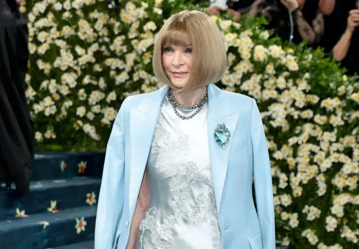 Anna Wintour, figura clave de que es la Gala Met, posa con un traje azul claro y un vestido blanco bordado, adornada con un collar y un broche de corazón.