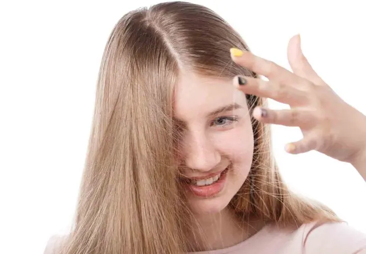 Chica sonriente con cabello rubio que se electrifica. Descubre cómo quitar la electricidad del pelo para un look suave.