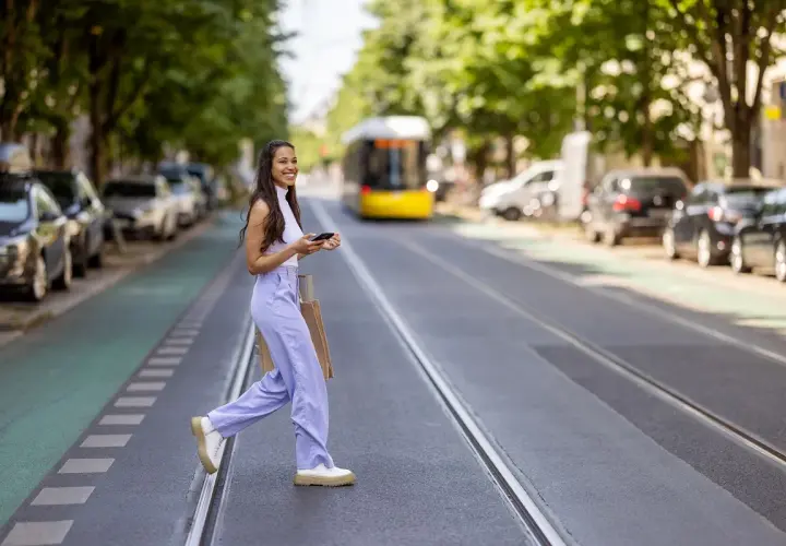 Mujer sonriente cruza la calle con bolsas, disfrutando de su estilo de slow fashion.