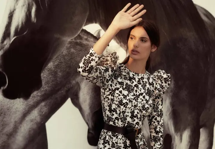 Inés Domecq, con su vestido floral, se protege del sol junto a la imponente silueta de un caballo.