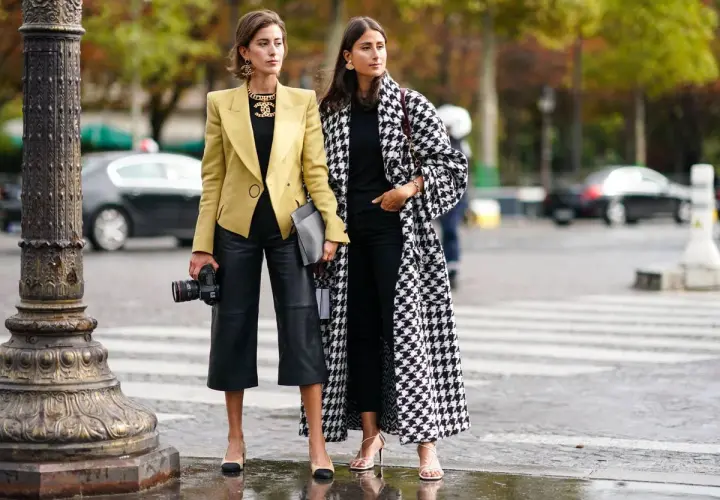 Dos mujeres con estilo muestran cómo vestir en otoño en España: una con blazer amarillo y pantalón culotte de cuero, la otra con abrigo de pata de gallo.