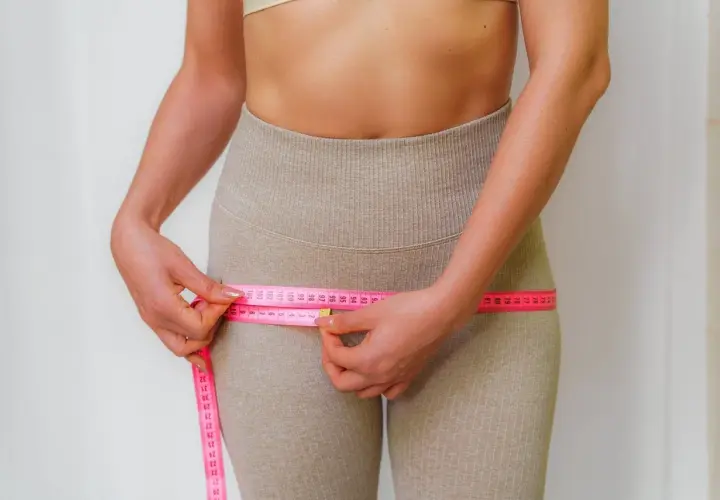 Mujer midiendo su cintura con cinta métrica rosa, enfocándose en la zona de los **hip dips**.