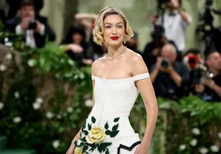 Gigi Hadid deslumbrante en la Met Gala, con un vestido blanco adornado con rosas amarillas y verdes.