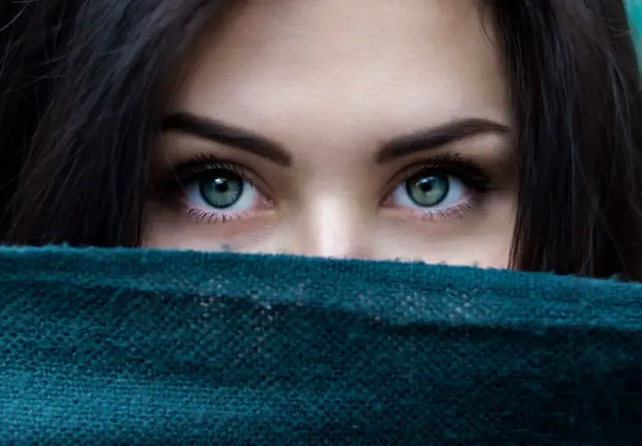 Ojos verdes penetrantes, enmarcados por cabello oscuro y un pañuelo. Un vistazo a la belleza que el microblading puede realzar.